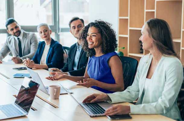 6 smiling people at a large table having a business meeting